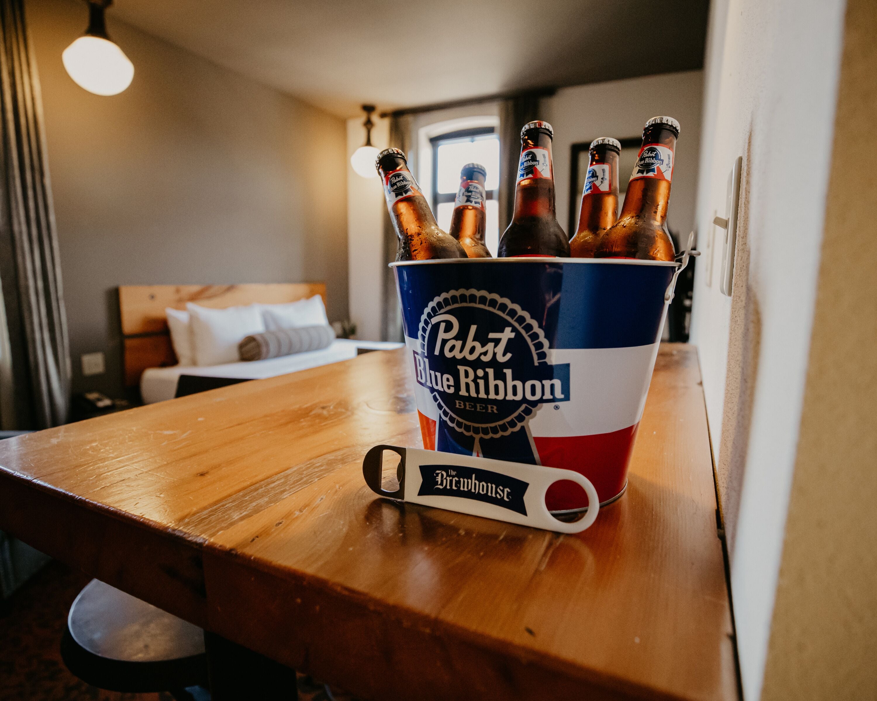 A bucket of Pabst Blue Ribbon beer on a wooden table in a hotel room.