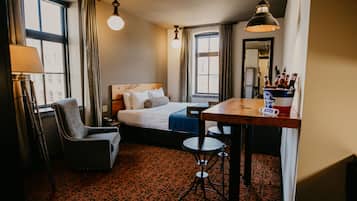A hotel room with a bed, a desk, a chair, a lamp, and a window.
