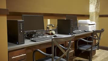 A hotel workspace with three computer stations, each with a monitor, keyboard, and mouse. There is a printer on the right side of the desk.