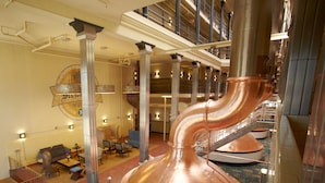 A lobby with a large copper spiral staircase, a seating area with sofas and tables, and a decorative wall with a circular emblem. - The Brewhouse Inn & Suites (Milwaukee)