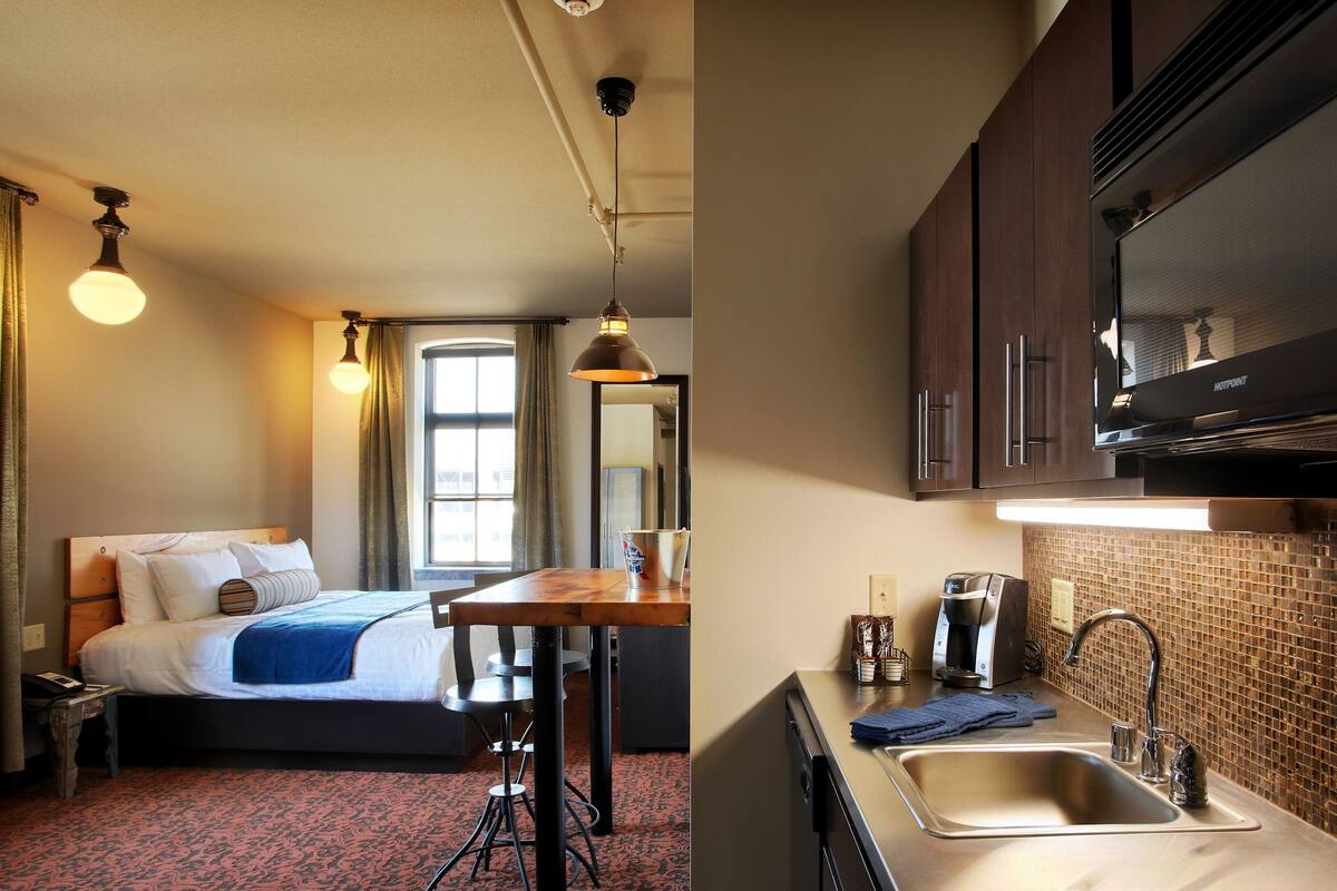 A hotel room with a bed, a desk, a coffee machine, and a sink.