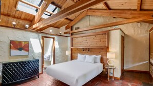 Un dormitorio con una cama grande, vigas de madera, chimenea de piedra y vistas a través de un ventanal.