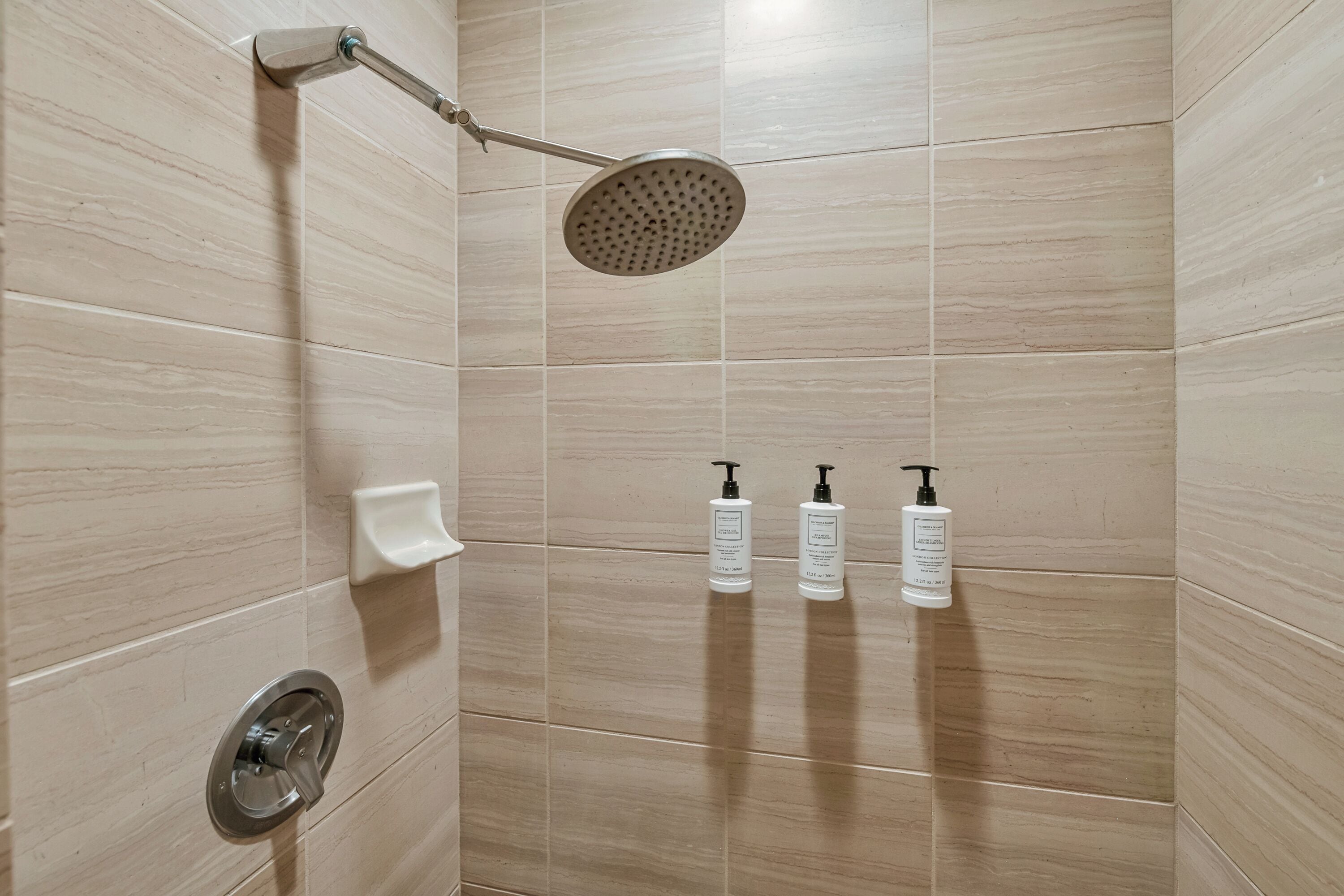 A shower area with a handheld showerhead, a soap dispenser, and two bottles of shampoo.