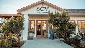 A building with a sign reading "SCV TASTING ROOM" at the entrance, surrounded by potted plants and barrels.