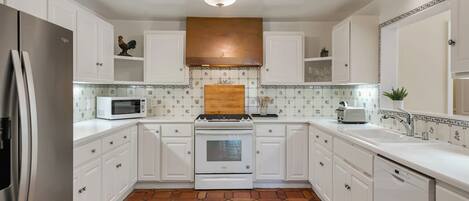 A kitchen with white cabinets, a stainless steel refrigerator, a microwave, a stove, and a sink.