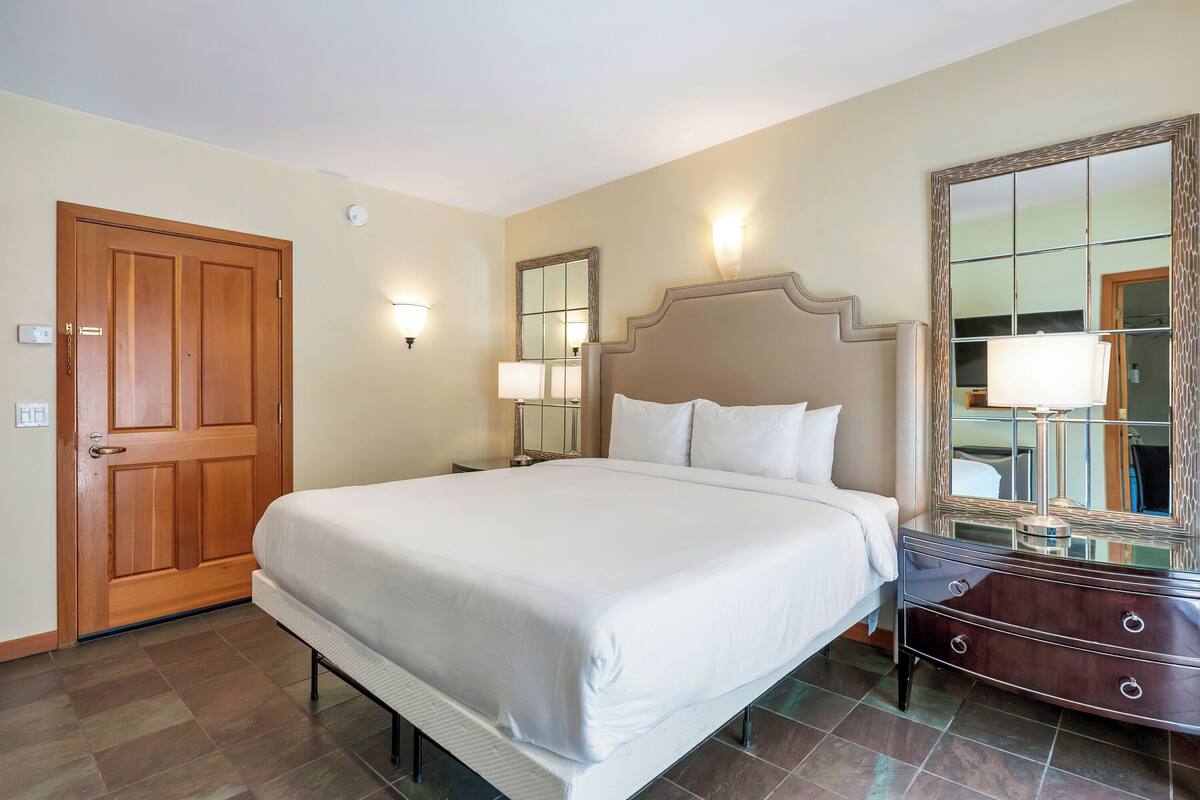 A hotel room with a large bed, a dresser, a mirror, and a door.