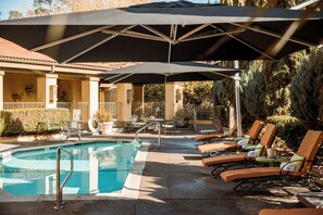 Zona junto a la piscina con sillones de descanso, sombrillas y una piscina.