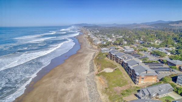 An aerial view of a coastal residential area with houses along the beach, clear skies, and distant mountains. - Cavalier Beachfront Condominiums (Lincoln City)