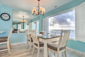 A dining area with a large window, a chandelier, and a clock on the wall. - Cavalier Beachfront Condominiums (Lincoln City)