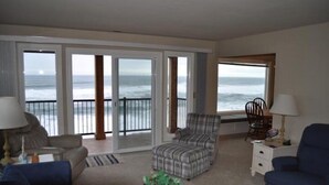 A living room with a view of the ocean, a sofa, a chair, a coffee table, and a lamp. - Cavalier Beachfront Condominiums (Lincoln City)