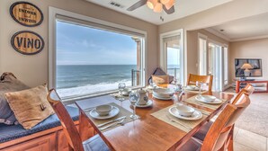 A dining area with a view of the ocean, a ceiling fan, and a table set for four. - Cavalier Beachfront Condominiums (Lincoln City)