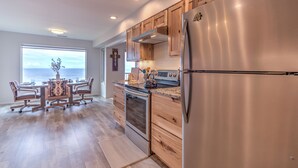 A modern kitchen with wooden cabinets, a stainless steel refrigerator, and a large window overlooking the ocean. - Cavalier Beachfront Condominiums (Lincoln City)