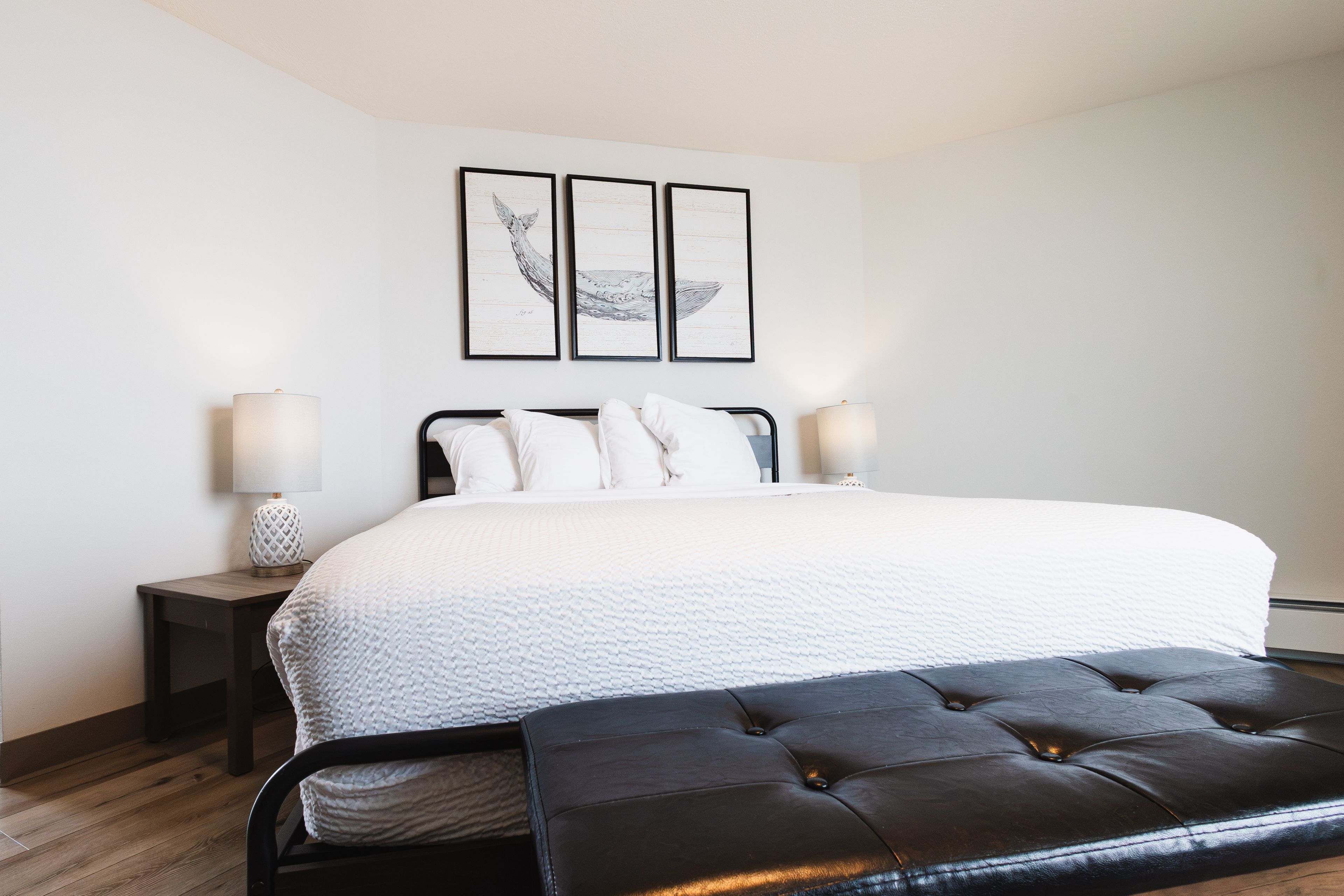 Une chambre à coucher comprenant un lit, des lampes de chevet, un banc et deux œuvres d’art accrochées au mur.