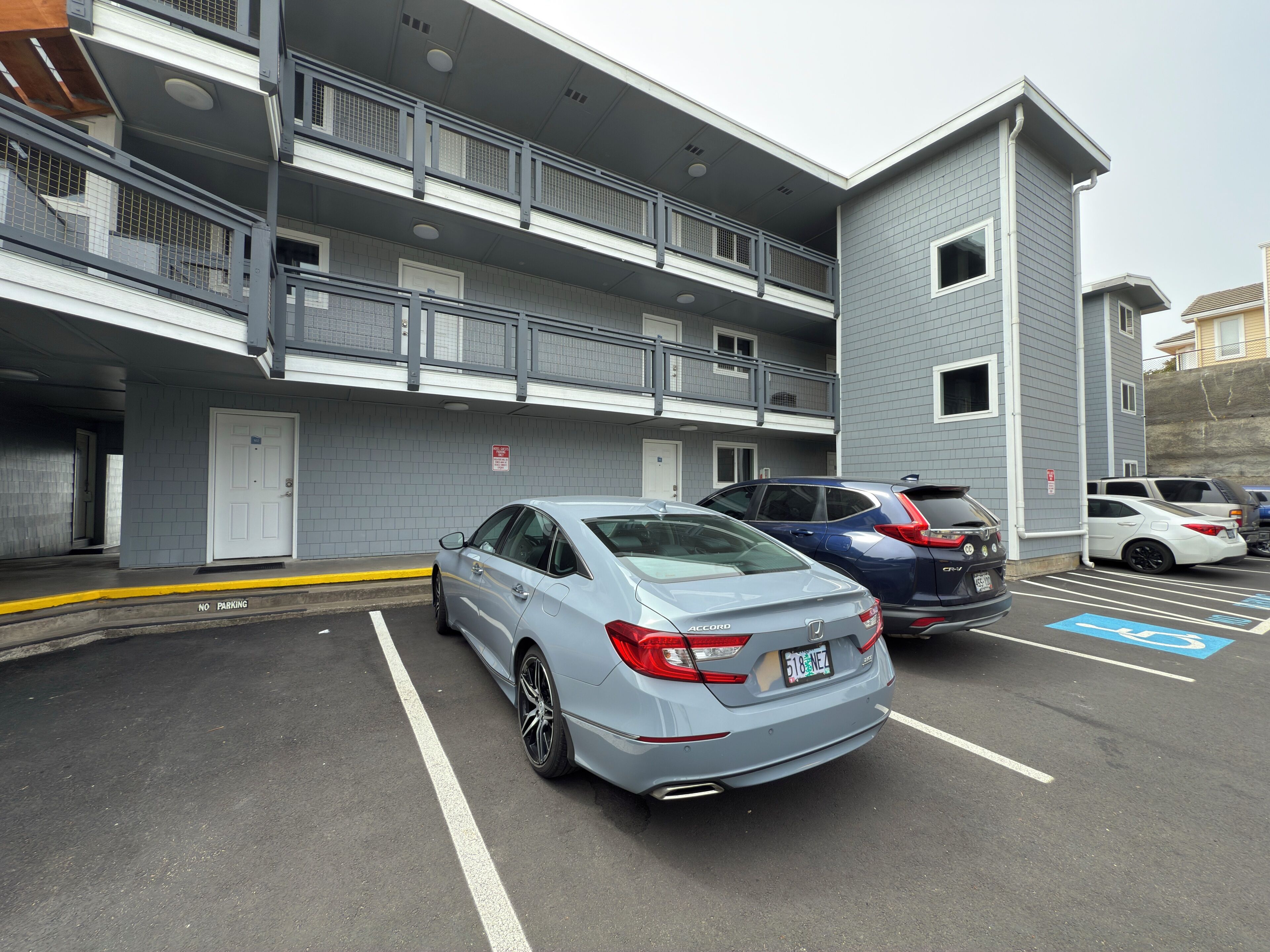 A parking area with a multi-story building, a white door, and several parked cars including a grey Honda Accord.