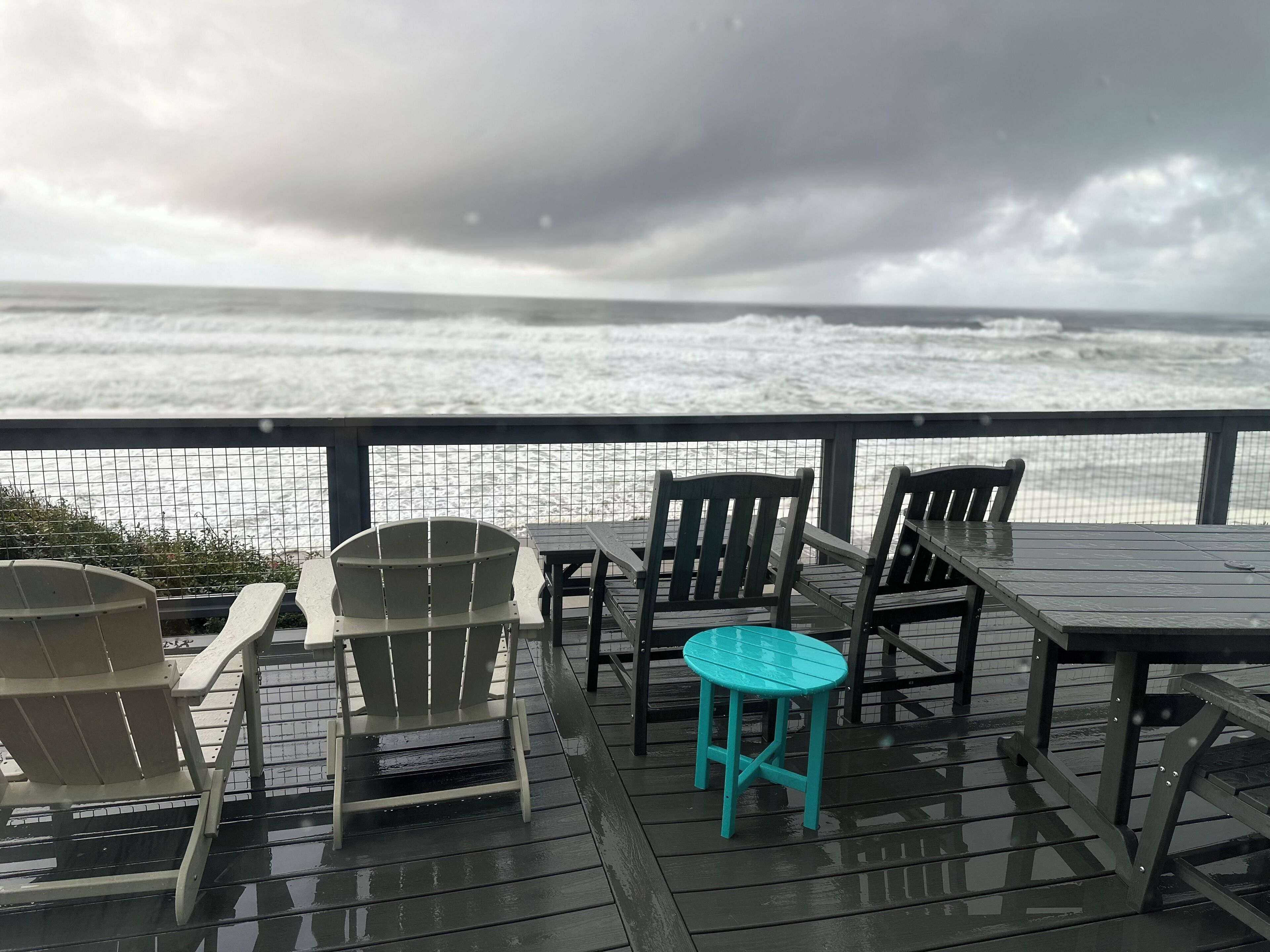 A wooden deck with chairs and tables overlooking the ocean.