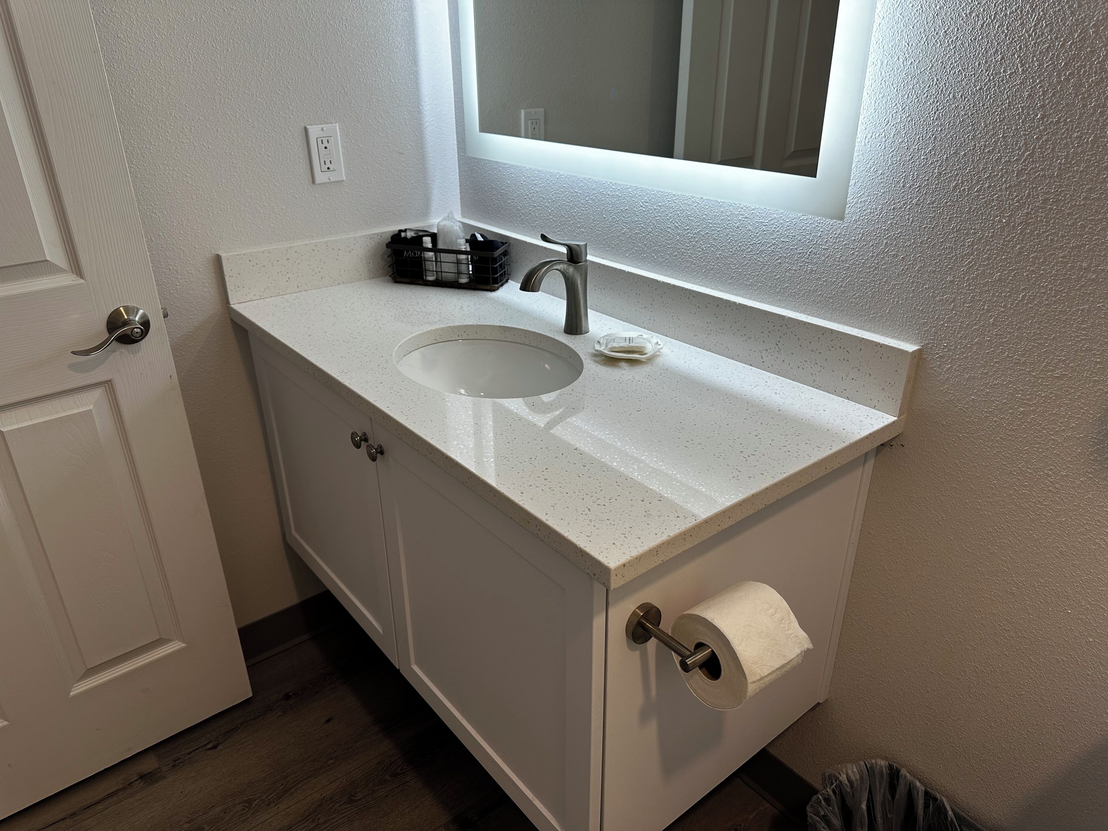 Une salle de bain avec un comptoir blanc, un lavabo, un miroir et un porte-rouleau de papier toilette.