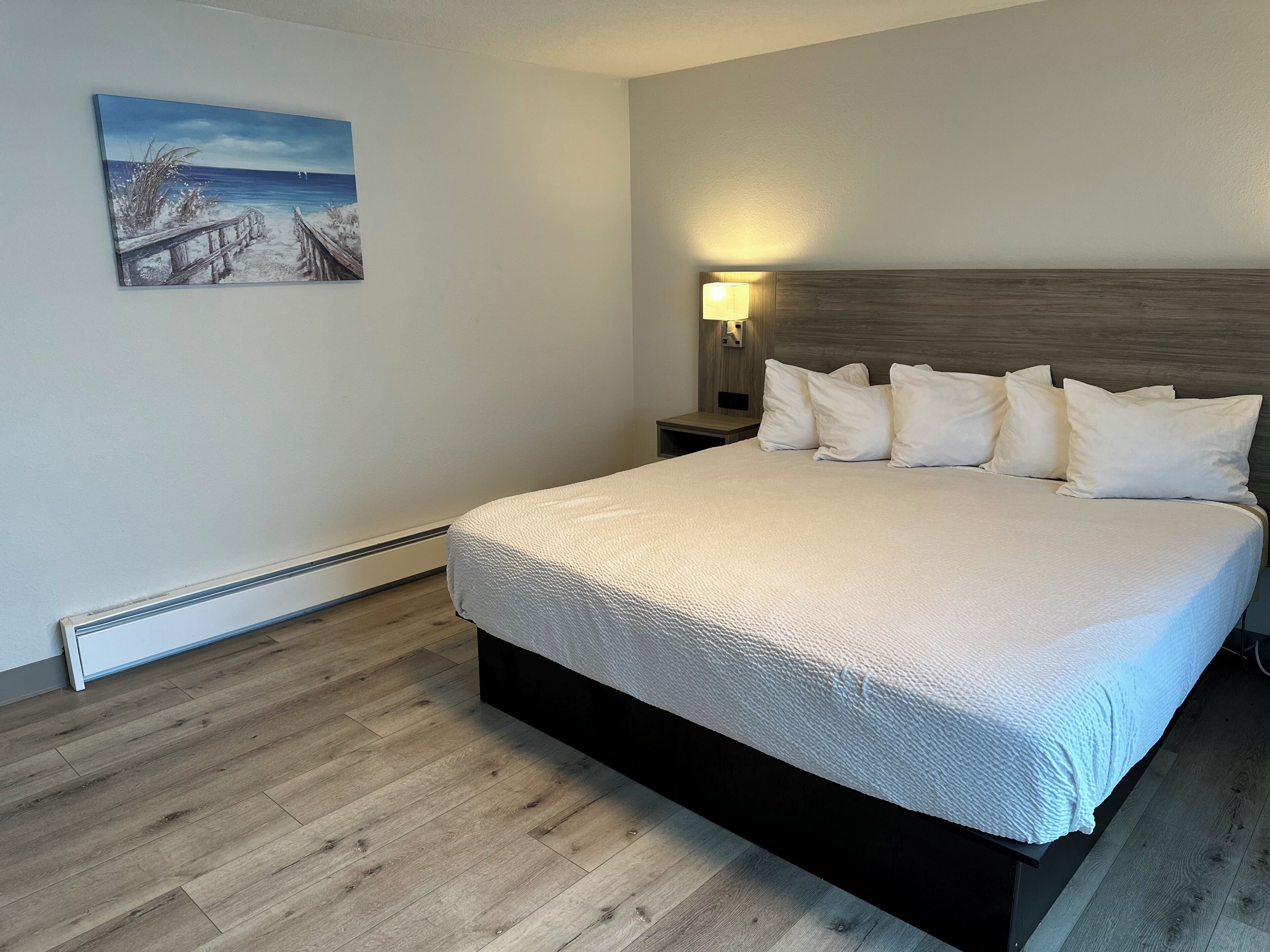 Un dormitorio con una cama grande, una mesita de noche con lámpara y un cuadro en la pared.