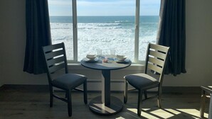 A room with a table and two chairs facing a large window with a view of the ocean. - West Beach Suites (Lincoln City)