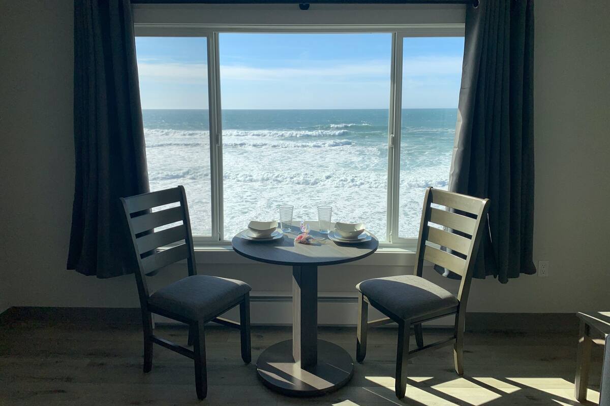 A room with a table and two chairs facing a large window with a view of the ocean.