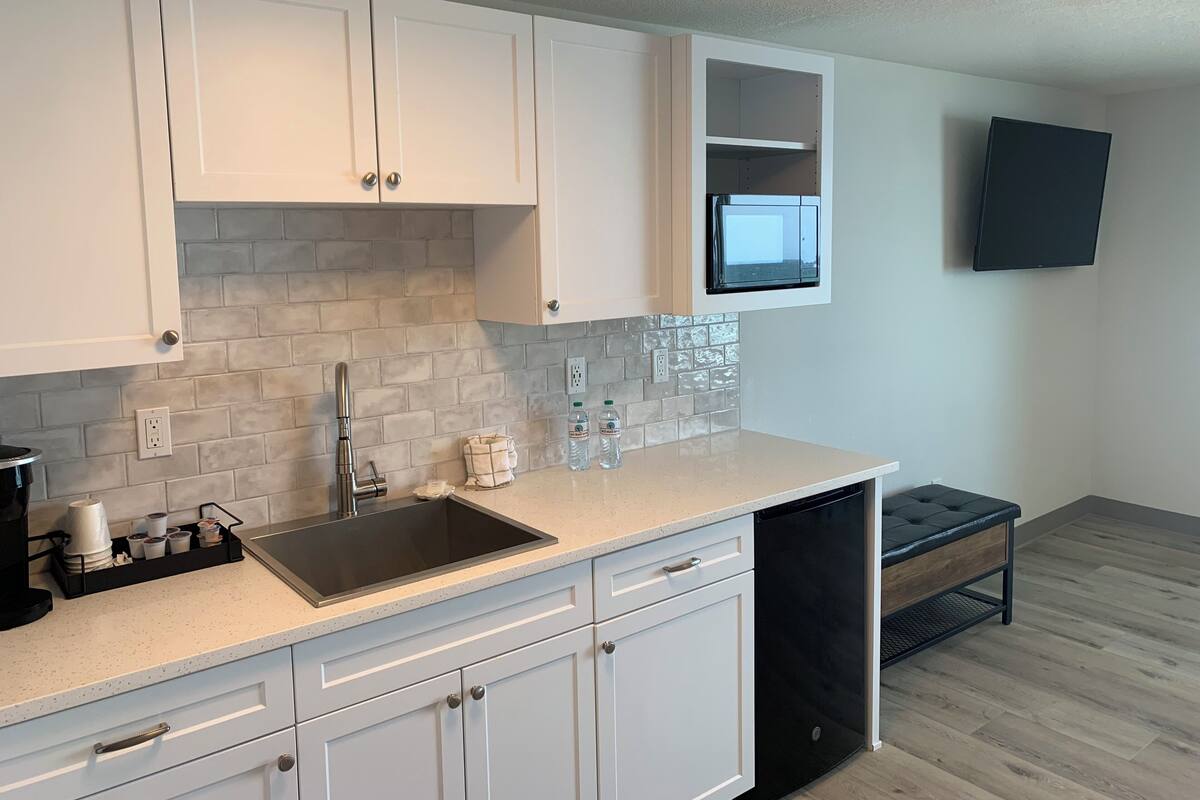 A modern kitchen with white cabinets, a stainless steel sink, a dishwasher, and a countertop with a water dispenser.