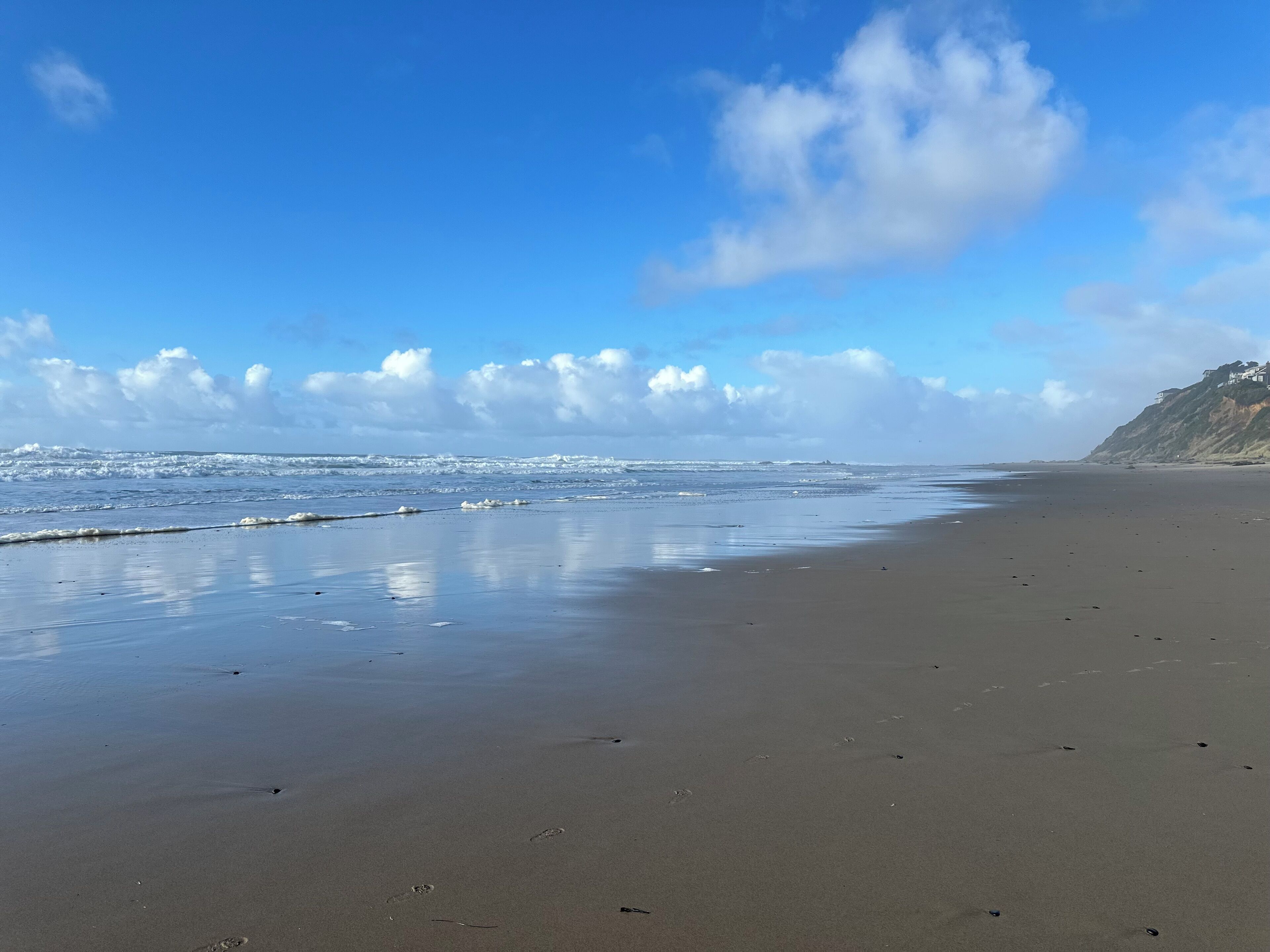 A wide sandy beach with gentle waves and a clear sky.