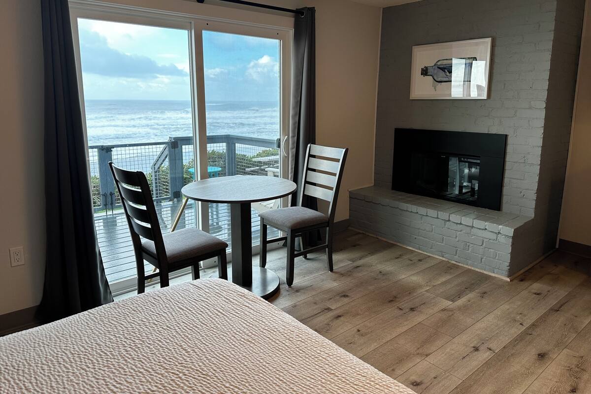 A balcony with a view of the ocean, a fireplace, and two chairs.