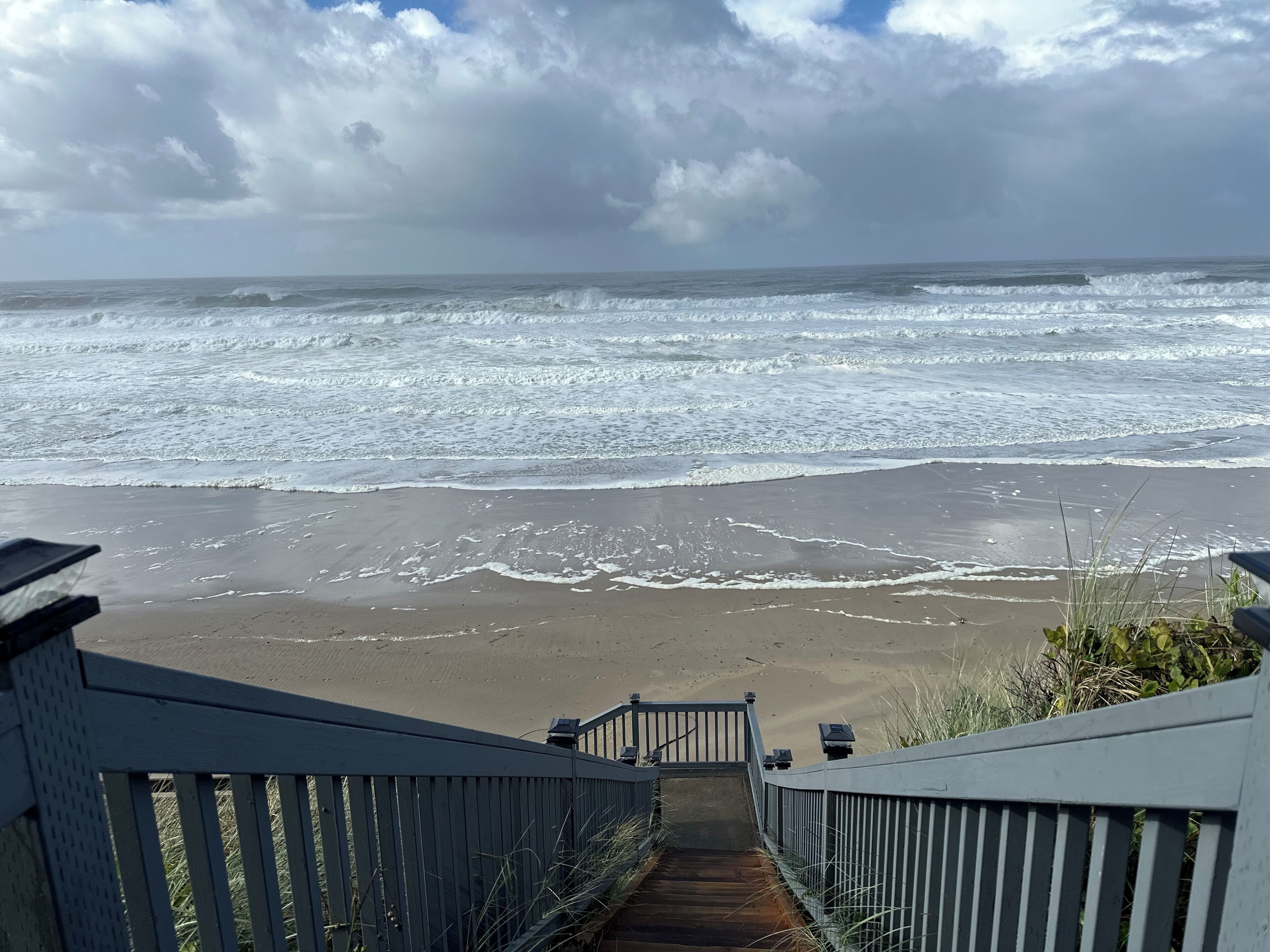 Una escalera de madera que lleva a una playa con olas rompiendo sobre la orilla.