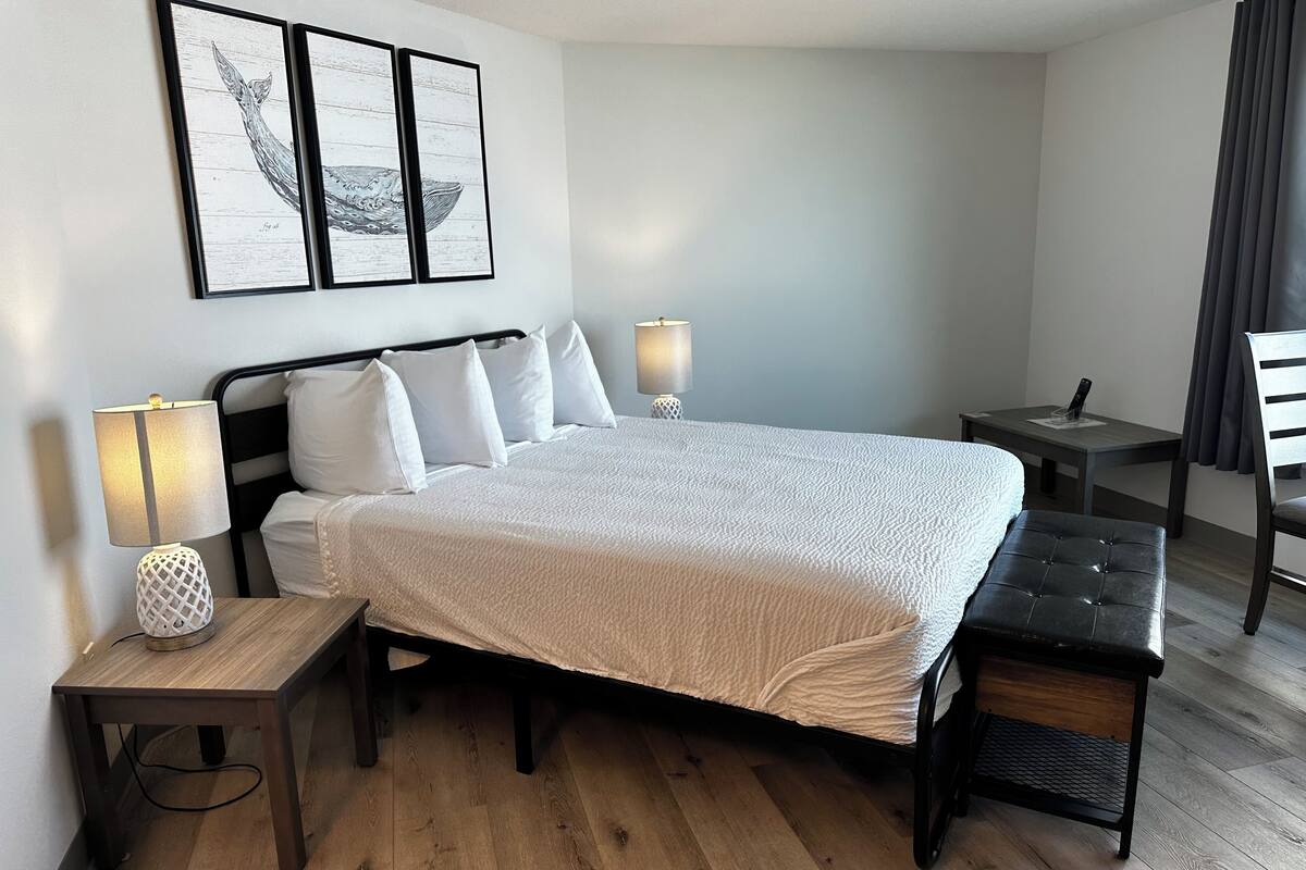 A neatly arranged hotel room with a large bed, bedside tables, a bench, and artwork on the wall.