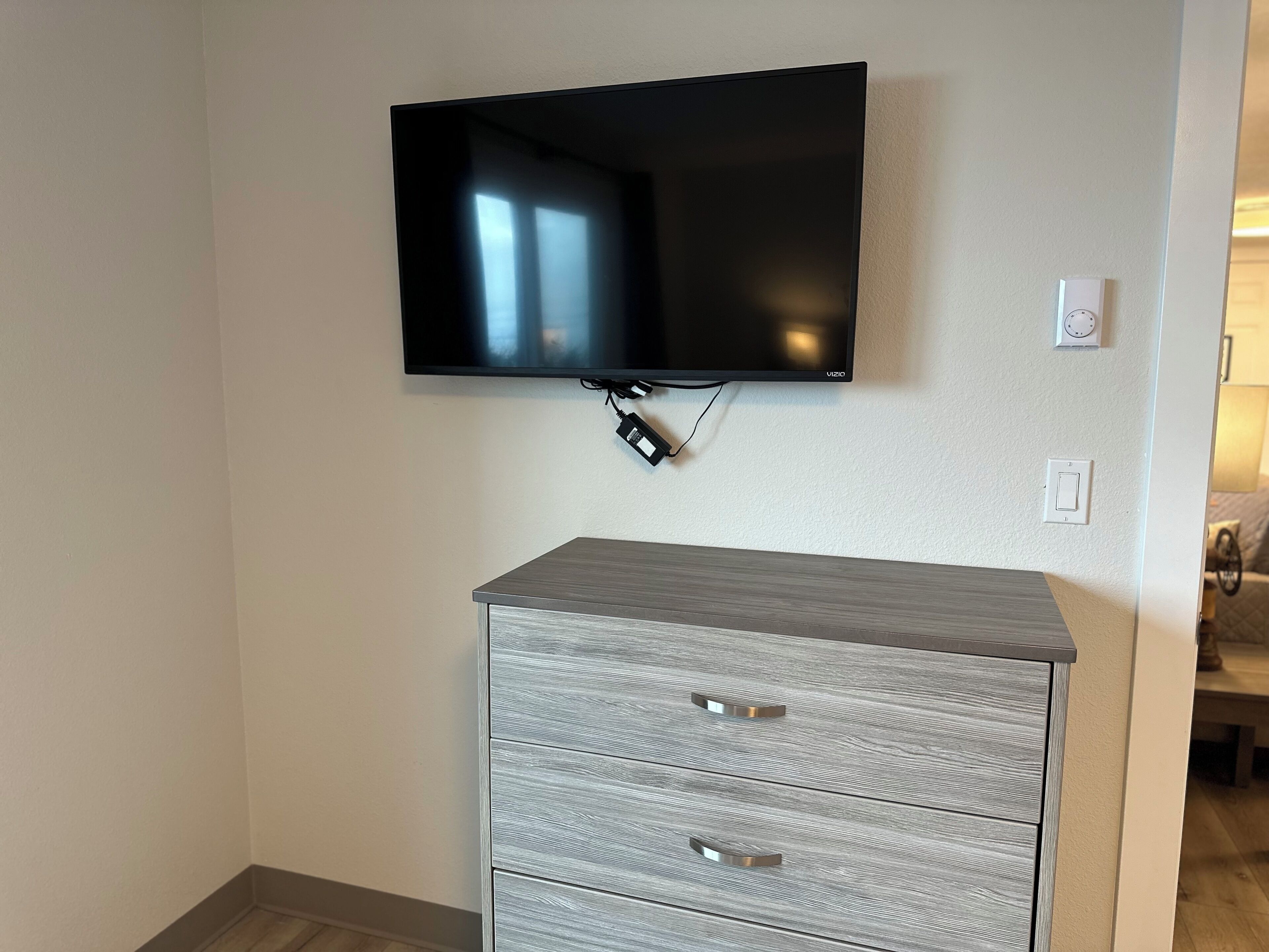 Un téléviseur à écran plat fixé au mur, au-dessus d’une commode grise dotée de poignées métalliques.