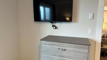 Un téléviseur à écran plat fixé au mur, au-dessus d’une commode grise dotée de poignées métalliques.