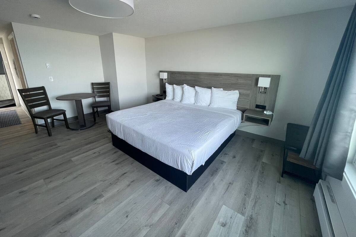 A hotel room with a large bed, a desk with a chair, a small table, and a lamp.
