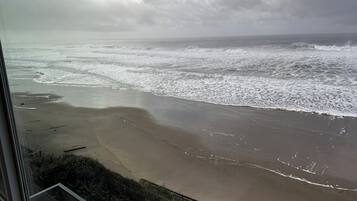 A view of a beach with waves from a window overlooking a grassy area.