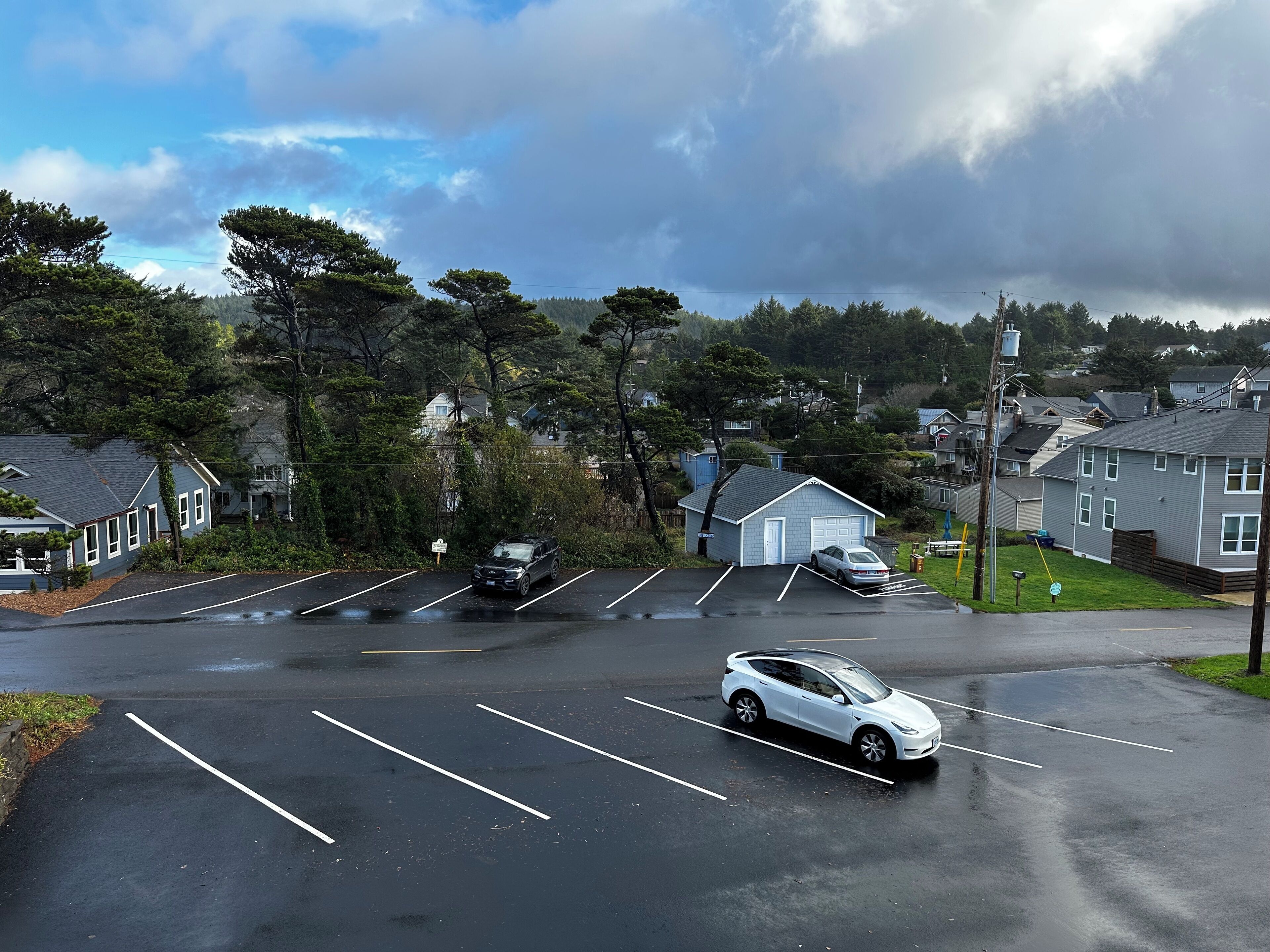 A parking lot with several cars, a small building, and houses in the background.