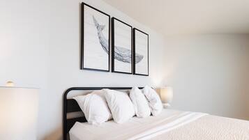 A neatly made bed with white bedding and pillows, a black metal headboard, and two wall-mounted picture frames with black frames.
