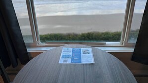 A brochure on a table by a window with a view of the beach. - West Beach Suites (Lincoln City)
