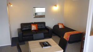 A compact room with a sofa, a single bed, a small table, and a chair. - Fernleaf Motel (Rotorua)