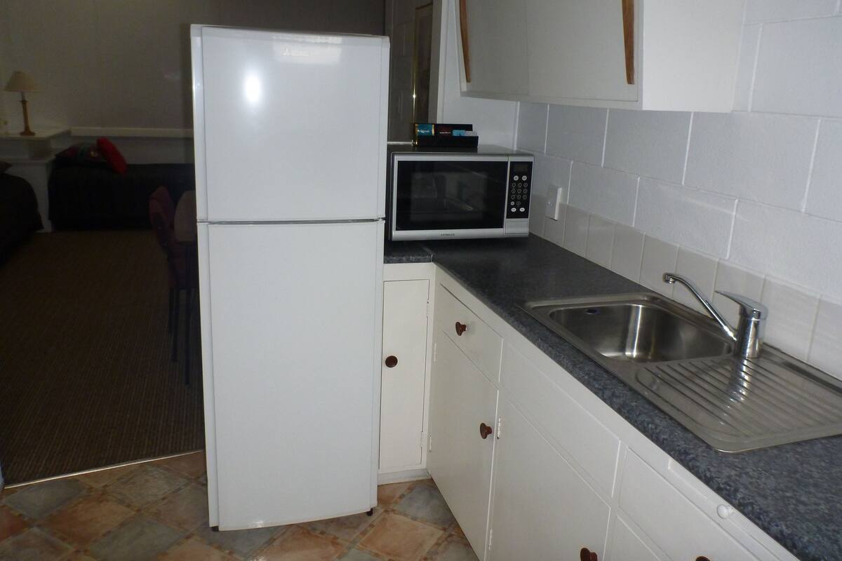A kitchen with white cabinets, a refrigerator, a microwave, and a sink.