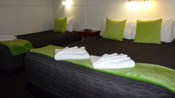 A hotel room with two beds, each with green and white pillows, and a nightstand with a lamp. - Fernleaf Motel (Rotorua)