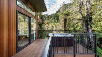 A wooden deck with a hot tub, surrounded by lush greenery and a mountain backdrop.