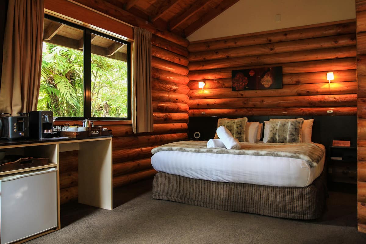 Una habitación tipo cabaña de madera con una cama, escritorio y un refrigerador pequeño.