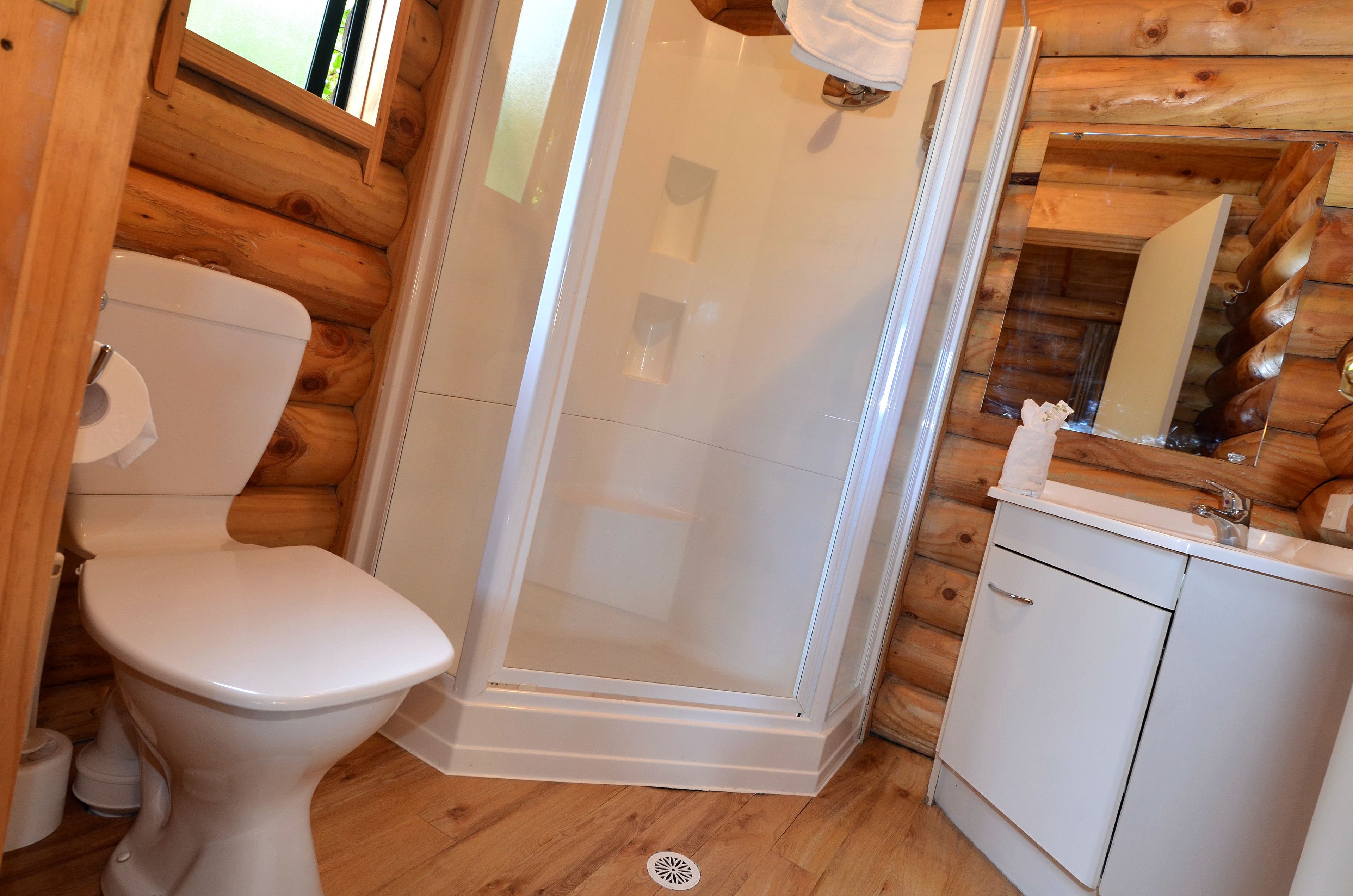 Ein Badezimmer in einer Holzhütte mit Toilette, Duschkabine und Waschbecken.
