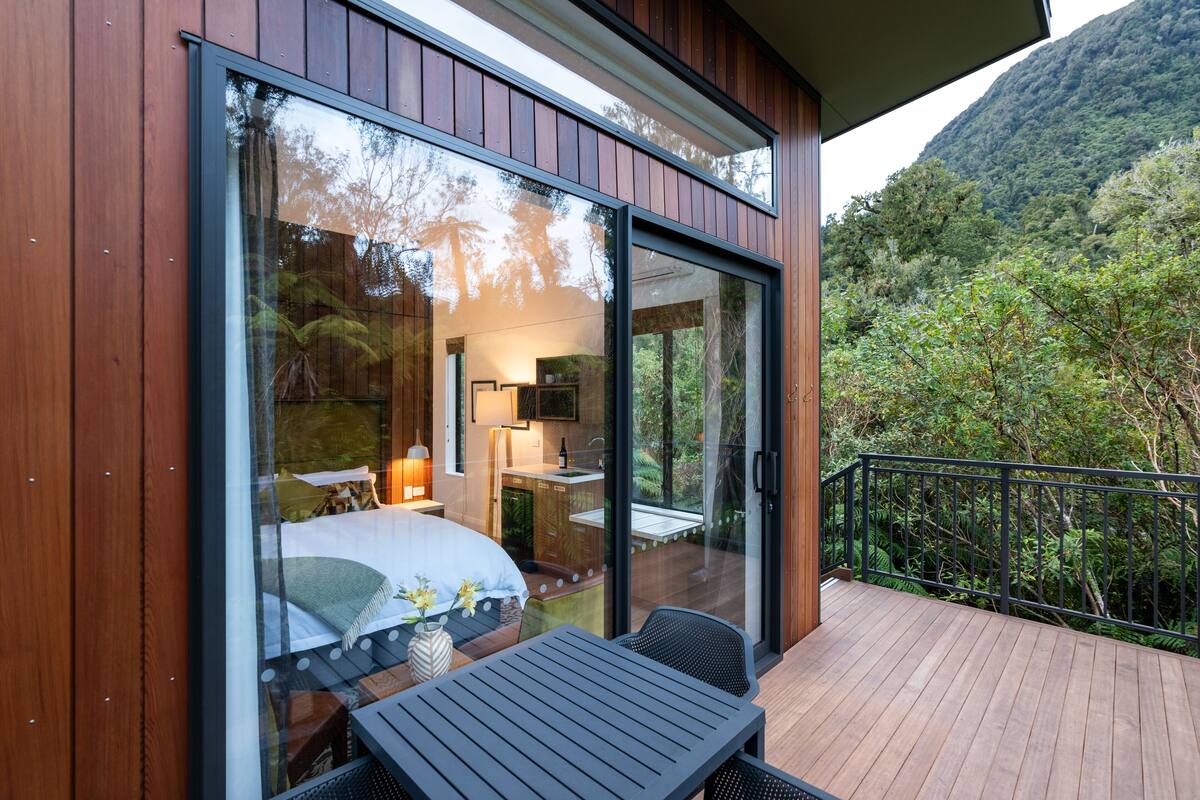 Un dormitorio moderno con un amplio ventanal, una terraza de madera y vistas a la montaña.