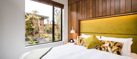 A bedroom with a large window, a bed with multiple pillows, and a wooden headboard.