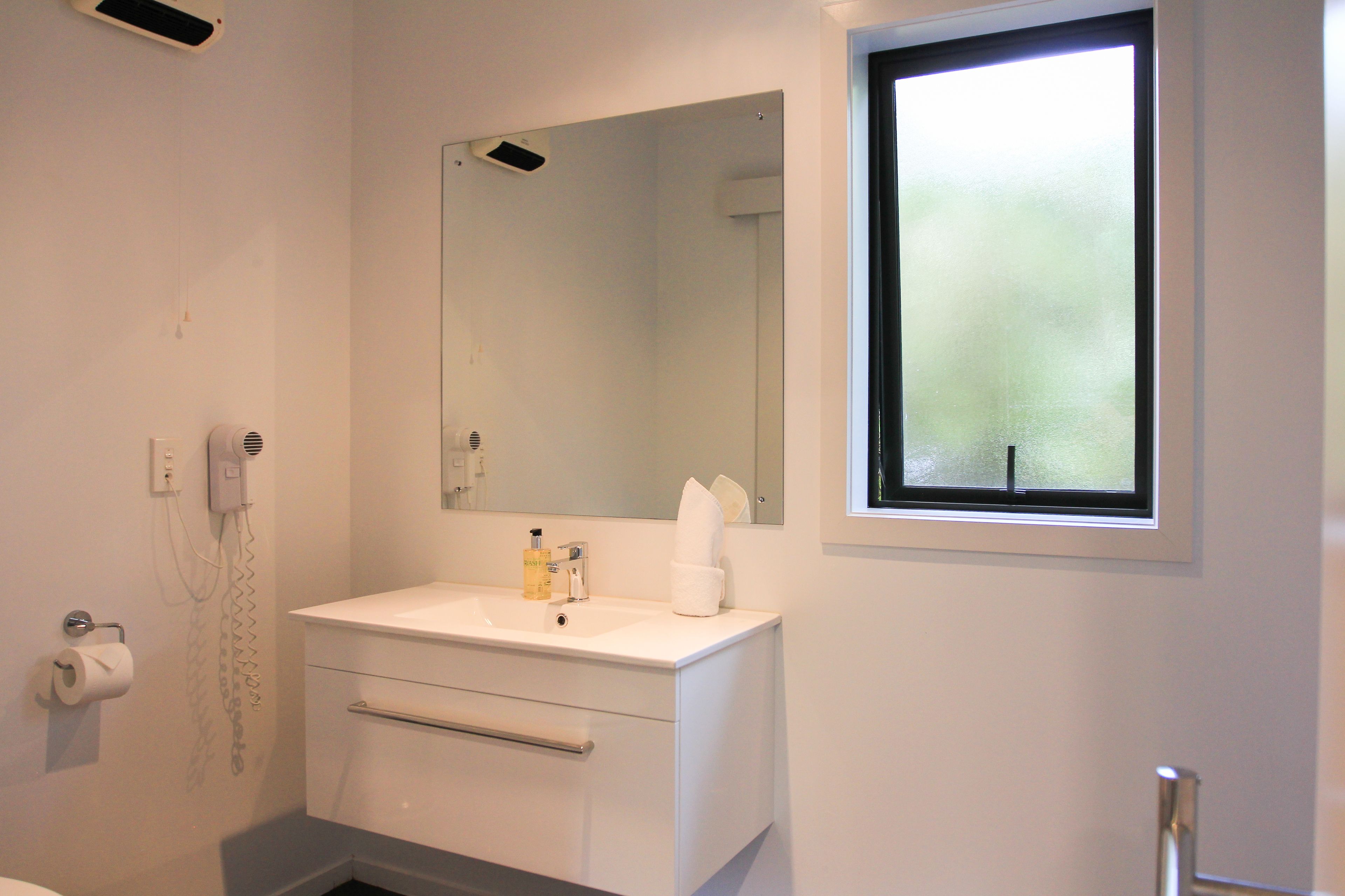 Een badkamer met een witte wastafel, een spiegel, een handdoek en een raam.