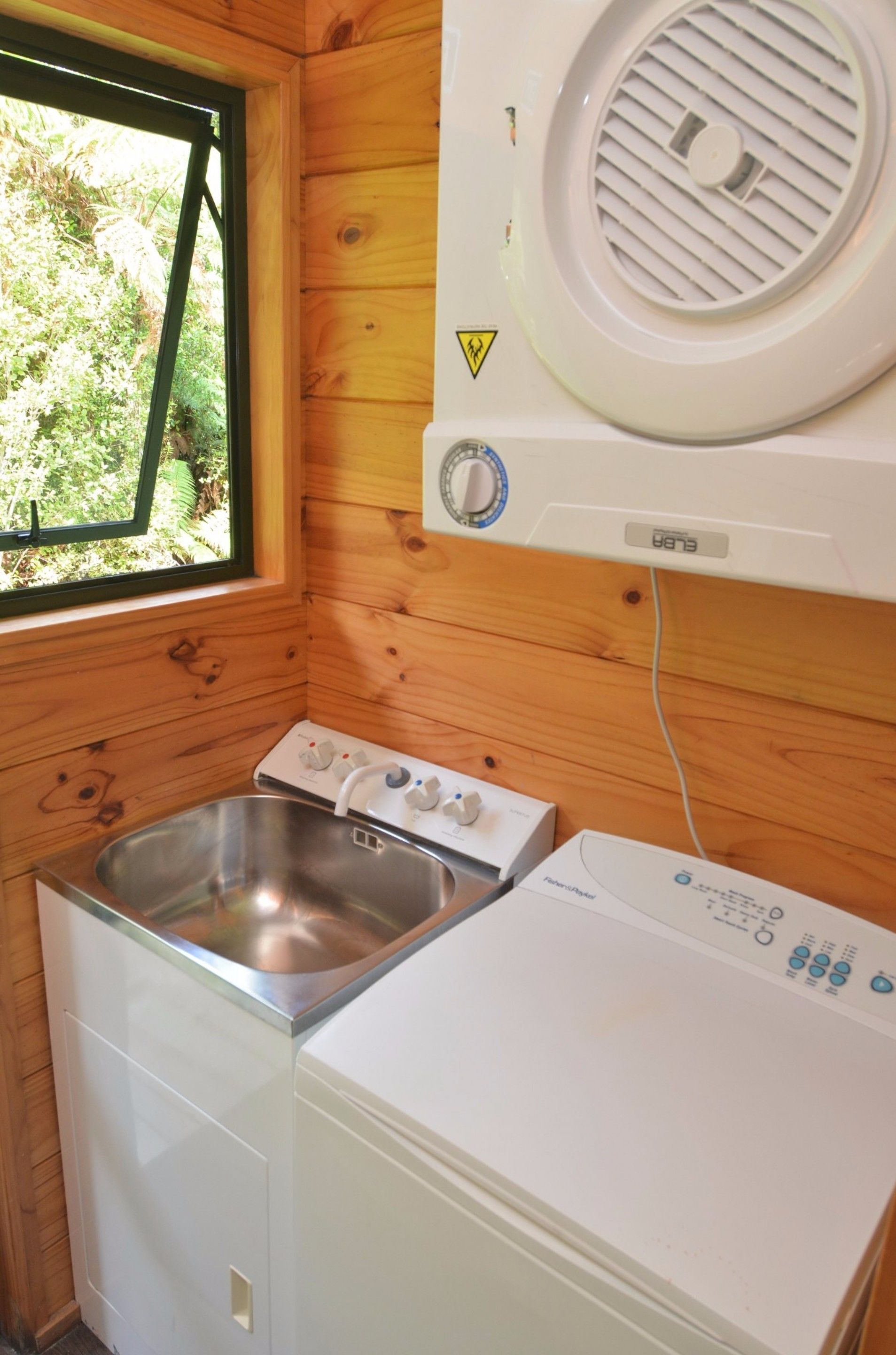 A compact kitchen with wooden walls, a window, a sink, and a washing machine.