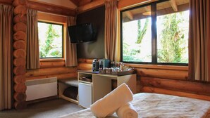 Una habitación acogedora tipo cabaña de troncos con un escritorio de madera, un televisor de pantalla plana, una pequeña kitchenette y un ventanal con vistas al follaje.