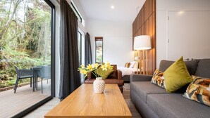 Una sala moderna con una mesa de centro de madera, un sofá con cojines estampados y vistas a una terraza y follaje exterior.