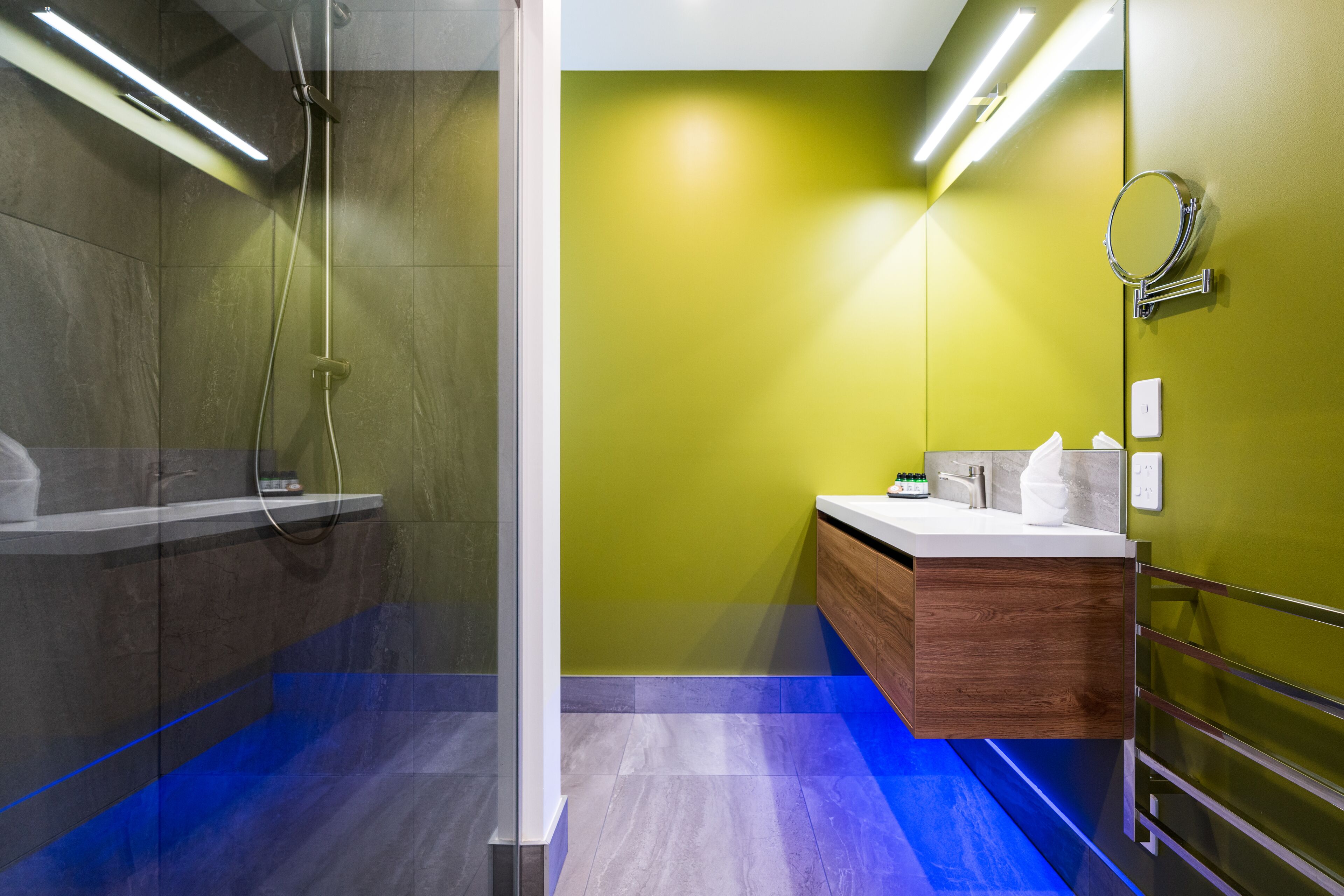 A modern bathroom with a shower, a vanity with a mirror, and a green accent wall.