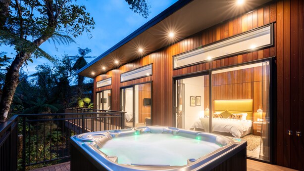 Un hotel moderno con jacuzzi en la terraza, fachada de madera y un dormitorio con cama y mesita de noche.