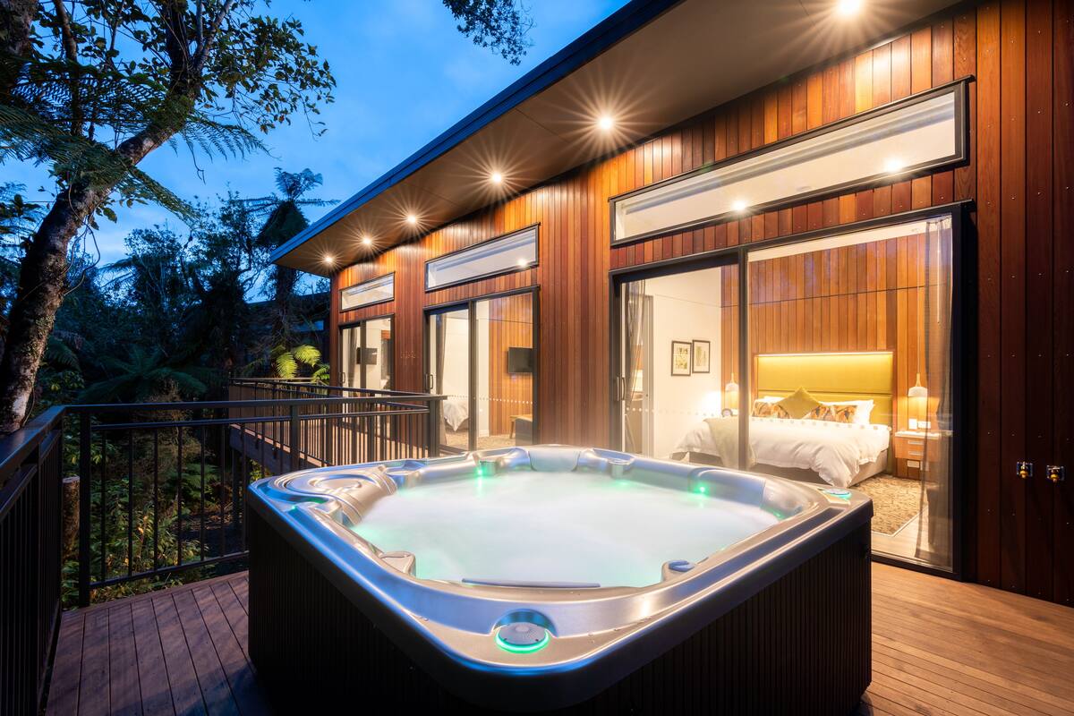 Un hotel moderno con jacuzzi en la terraza, fachada de madera y un dormitorio con cama y mesita de noche.